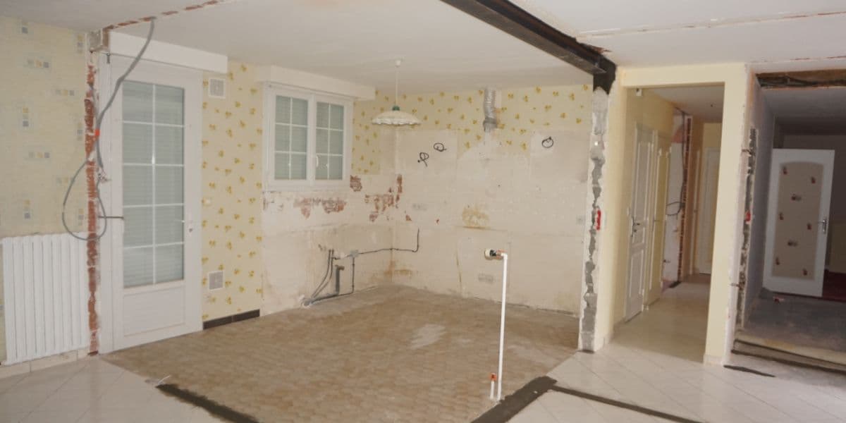 Pièce en rénovation avec murs partiellement dénudés, tuyauterie apparente et fils électriques visibles.