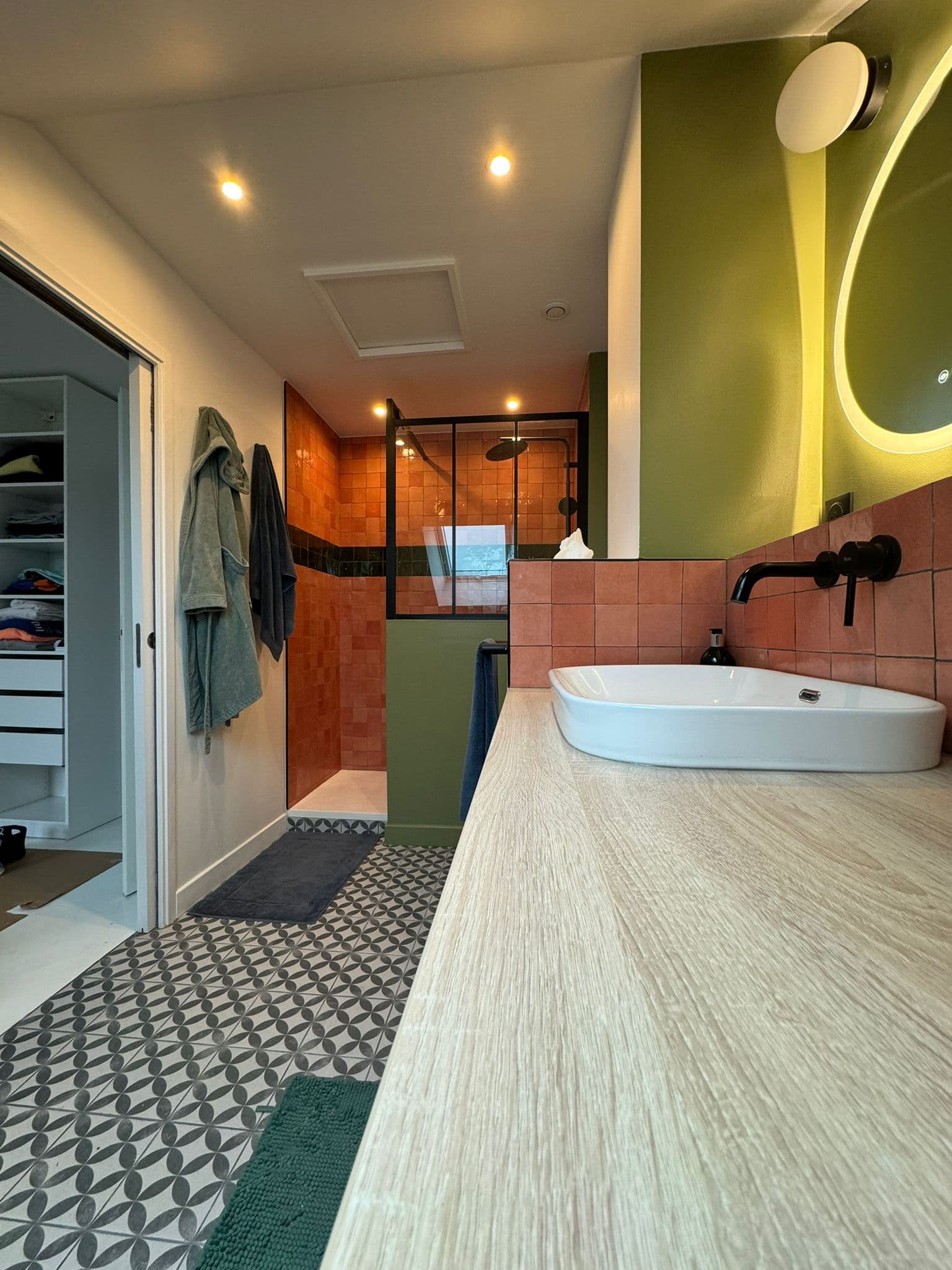 Salle de bain moderne avec vasque blanche, carrelage terre cuite et sol à motifs géométriques.