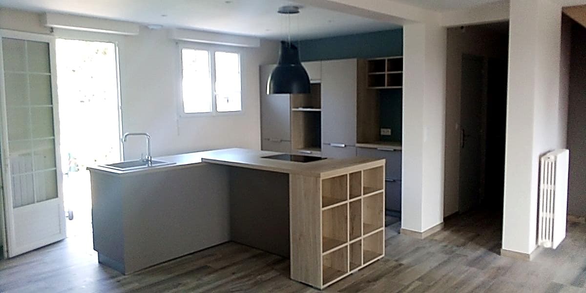 Cuisine moderne avec îlot central gris, étagères en bois clair et luminaire suspendu noir.